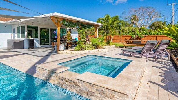 Une piscine agrémentée d’une pergola et de chaises longues, entourée d’une clôture en bois et de plantes tropicales.