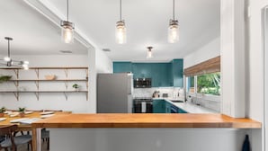 Une cuisine moderne avec des armoires de couleur turquoise, un îlot central en bois et des luminaires suspendus.