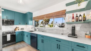 Une cuisine moderne avec des meubles de couleur turquoise, un lave-vaisselle noir et une machine à café.