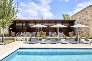 Zona de piscina con sillones de descanso, sombrillas y una terraza de madera.
