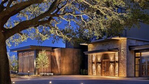 A modern building with a stone facade and large wooden doors, surrounded by trees and a well-lit entrance. - King Room at a 5⭐️ Hotel (Frisco)