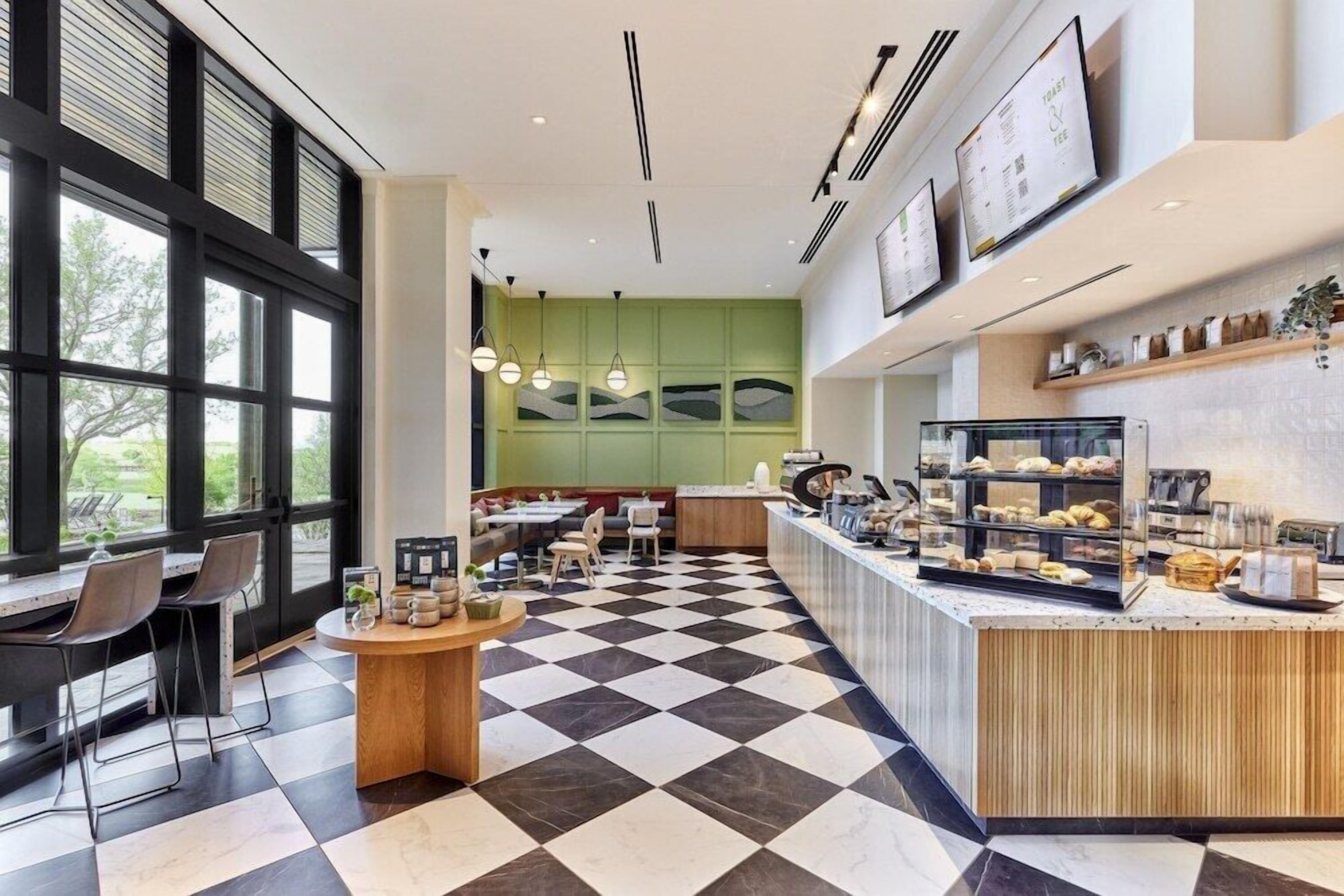 A modern cafe with a checkered floor, wooden counter, and seating area with tables and chairs.