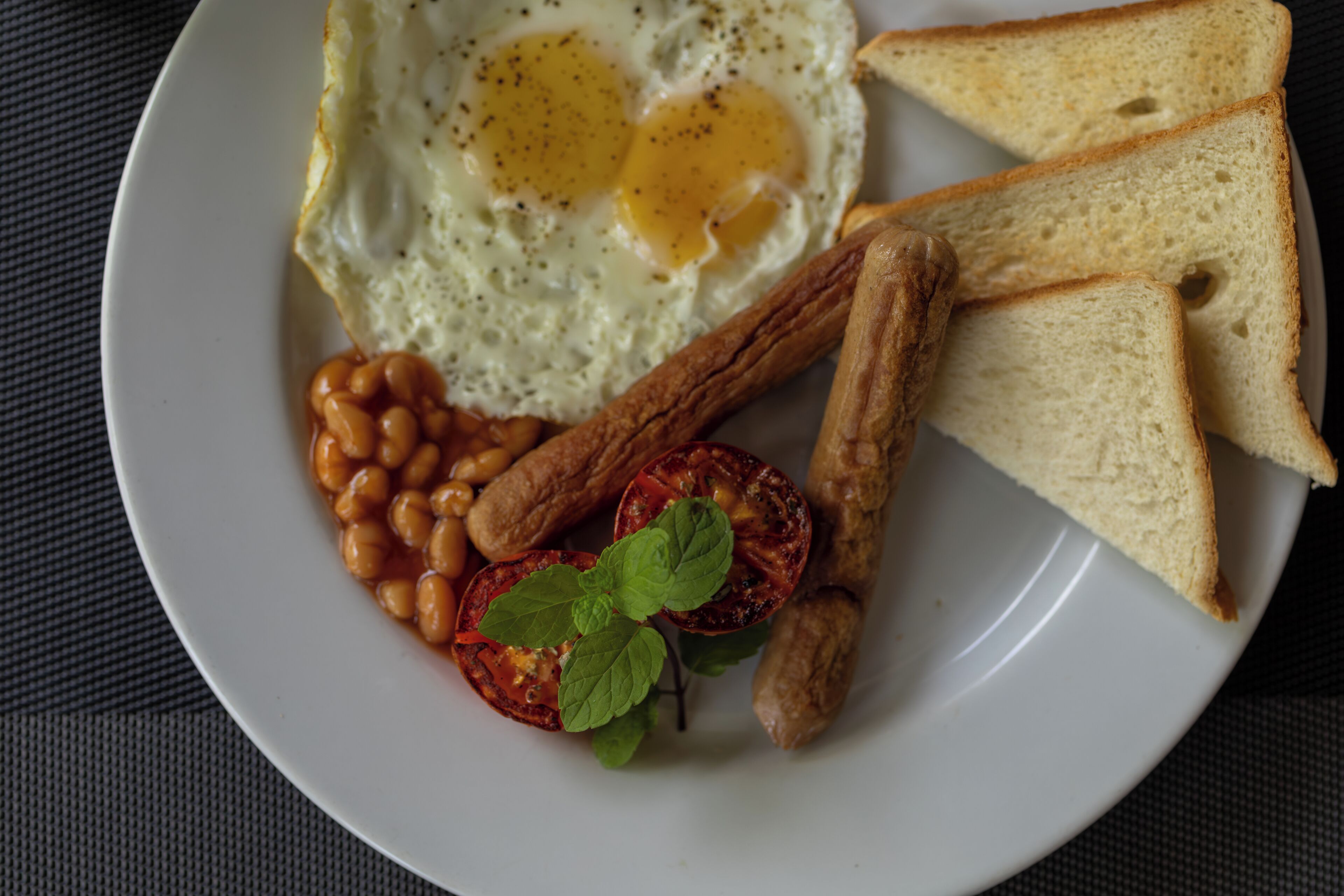 Un plato con huevos fritos, frijoles, tostadas y una rodaja de tomate.