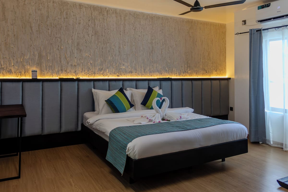 Ein modernes Hotelzimmer mit einem großen Bett, Holzboden, Deckenventilator und Blick ins Freie durch ein Fenster.