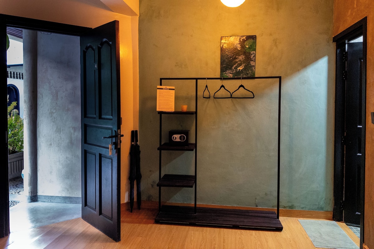 Ein Zimmer mit schwarzem Kleiderschrank, einer kleinen Ablage mit Radio und einem Haken für Jacken.