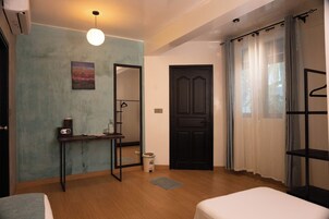 Una habitación con cama, escritorio con silla, espejo, puerta y ventana con cortinas.