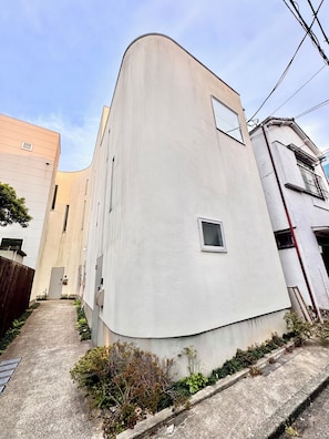 A narrow alleyway with a curved building, a small window, and a door.