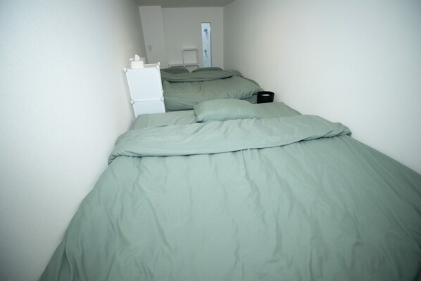 Una habitación pequeña con una cama, un armario blanco y un bote de basura negro.