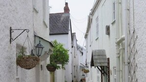 A narrow cobblestone alley between white buildings with hanging baskets and potted plants. - The Pepper Pot Sleeps 4 Sunlit Garden (Exmouth)