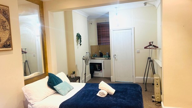 Un dormitorio con cama, mesita de noche, espejo, cómoda, ventilador y puerta que da al baño.