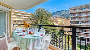 A balcony with a table set for two, overlooking a cityscape with buildings and a mountain.
