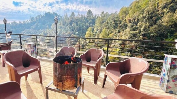 Una terrazza con sedie di plastica e un braciere in metallo, con vista su una valle boscosa.