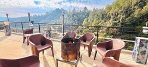 A terrace with plastic chairs and a metal fire pit, overlooking a forested valley. - Yashvi Paradise Shimla (Shimla)