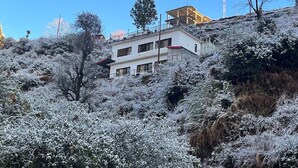 Un edificio a due piani con un balcone al piano superiore, circondato da vegetazione innevata.