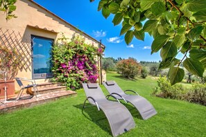 A sunny outdoor area with a pool, lounge chairs, and a building with a window and a door.