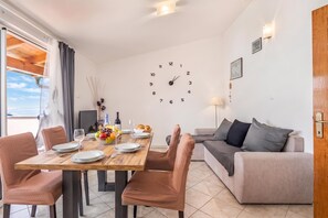 Un salon moderne avec un coin repas, comprenant une table à manger en bois pour deux personnes, un canapé et une horloge murale.