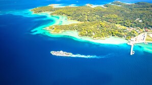 An aerial view of a coastal area with a cruise ship docked near a pier, surrounded by turquoise waters and lush green islands.