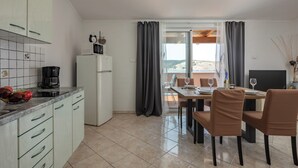 A modern kitchen with a dining area, a refrigerator, a coffee maker, and a view of the outdoors. - Sunset By The Sea /w Sea View Balcony, Lopar, Croatia (Lopar)