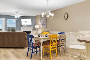 A dining area with a white table, colorful chairs, a chandelier, and a television on the wall. - Freshly Updated Lake-Access Condo with Outdoor Pool, Mini Golf, Pickleball & Free Attraction Tickets (Kimberling City)