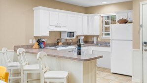 A kitchen with white cabinets, a central island with bar stools, a microwave, and a refrigerator. - Freshly Updated Lake-Access Condo with Outdoor Pool, Mini Golf, Pickleball & Free Attraction Tickets (Kimberling City)