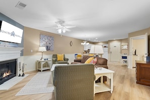 A living room with a fireplace, a television, and a ceiling fan.