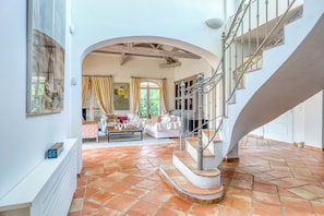 A spacious living area with a tiled floor, a white sofa set, and a staircase with ornate railings.