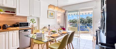 A modern kitchen with white cabinets, a dining table set for four, and a view of a balcony with a blue railing.