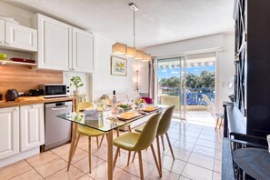 A modern kitchen with white cabinets, a dining table set for four, and a view of a balcony with a blue railing.