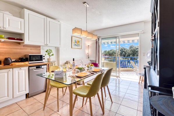 A modern kitchen with white cabinets, a dining table set for four, and a view of a balcony with a blue railing.