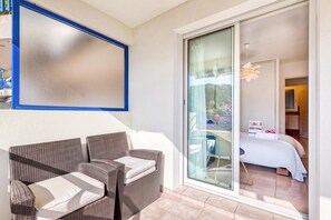 A balcony with wicker furniture and a sliding glass door leading to a bedroom with a bed and a nightstand.