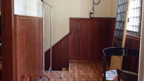 A hallway with wooden paneling, a metal handrail, a chair, and a window with bars. - Dimocrata (Phnom Penh)
