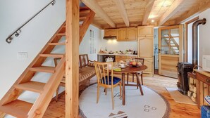 Een houten interieur met een trap, een eetgedeelte met een ronde tafel en stoelen, en een keuken met houten kasten en een fornuis.