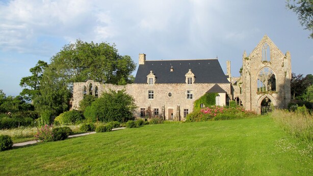 A historic stone building with a large garden and a ruined tower.