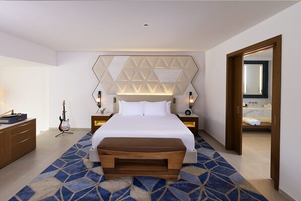 Ein modernes Hotelzimmer mit einem großen Bett, einem Teppich mit geometrischem Muster, Nachttischlampen und einer Gitarre auf einem Ständer.