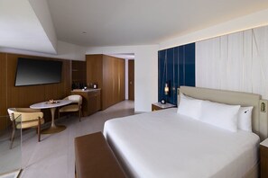 Ein modernes Hotelzimmer mit einem großen Bett, einem Schreibtisch mit Stuhl, einem an der Wand befestigten Fernseher und einer Minibar.