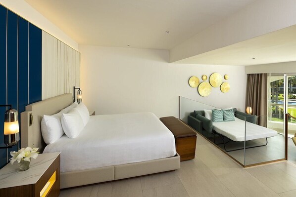 Ein modernes Hotelzimmer mit einem großen Bett, einer Schlafcouch, einer Glastrennwand und Blick ins Freie.