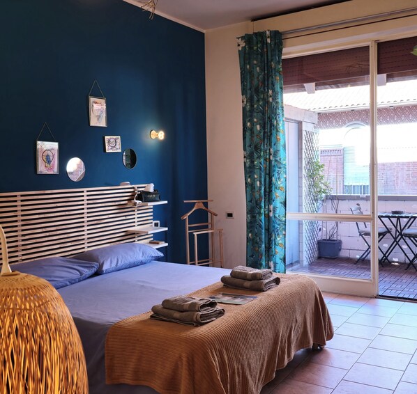 Une chambre à coucher avec un lit, des tables de chevet, une lampe suspendue et une vue sur le balcon extérieur.