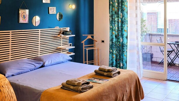 A bedroom with a bed, bedside tables, a hanging light fixture, and a view of the outside through a window with curtains. - Gorgeous apartment near the metro (Torino)