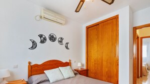 Un dormitorio con una cama de madera, una mesita de noche con lámpara, aire acondicionado de pared y un armario de madera.