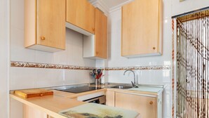 Una cocina compacta con armarios de madera, horno integrado y una pequeña encimera con tabla de cortar.