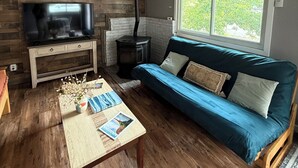 Un salon avec un téléviseur, des murs en bois, un canapé bleu et une fenêtre.