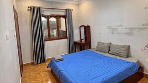 Un dormitorio con cama, suelo de madera, ventana con cortinas, espejo y luz de techo.