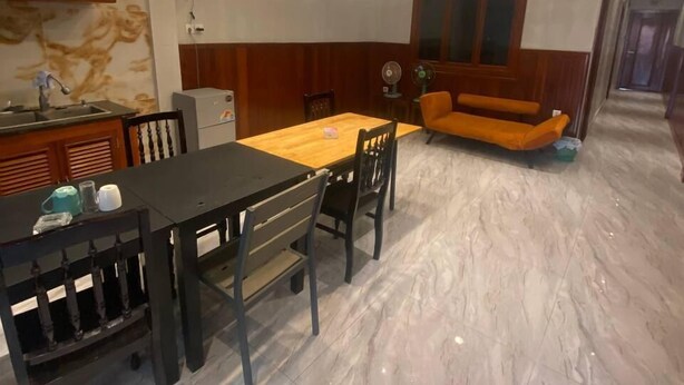 Comedor con piso de mármol, mesa y sillas de madera. Hay lámparas colgantes, un sofá y un aparador.