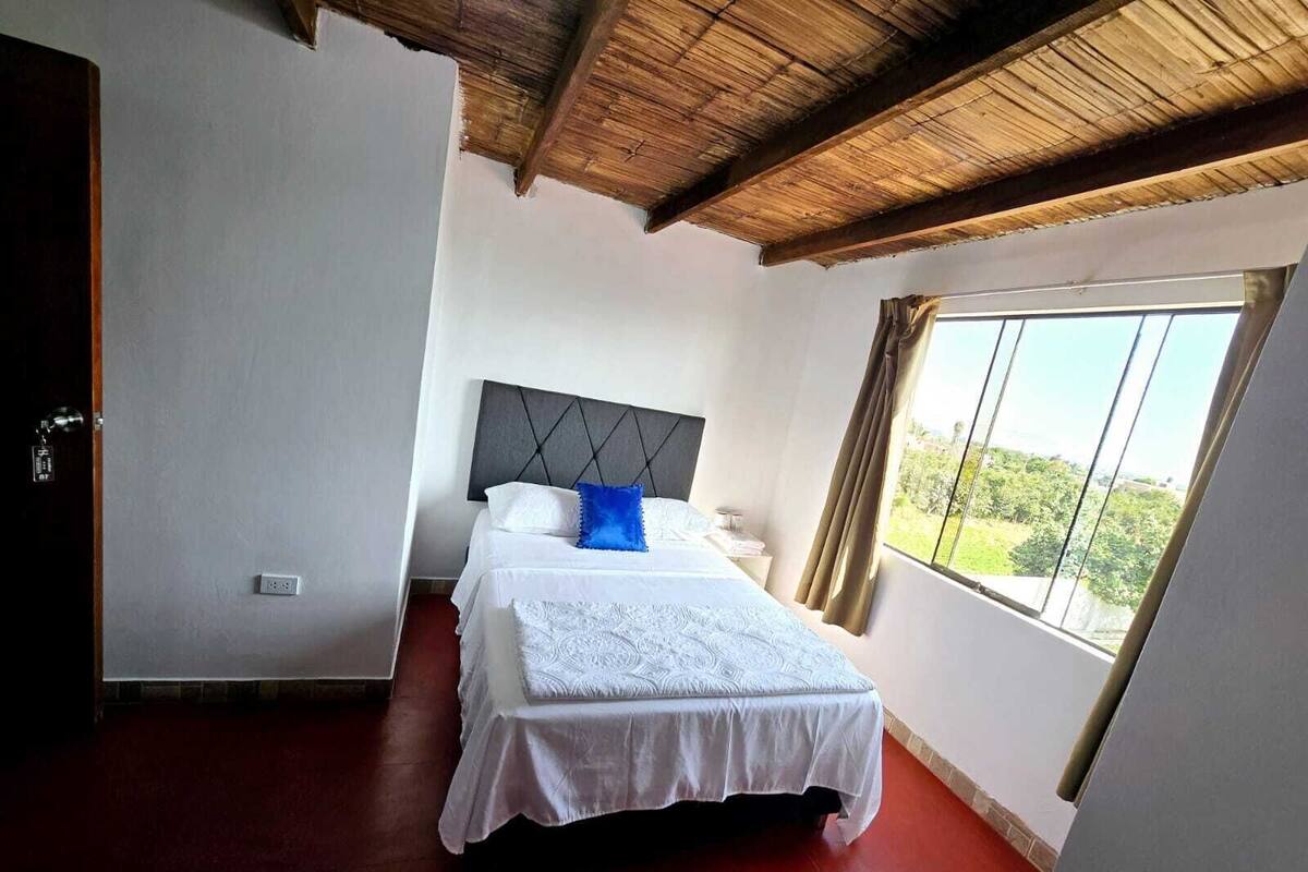 A bedroom with a bed, a window with a view, and a wooden ceiling.
