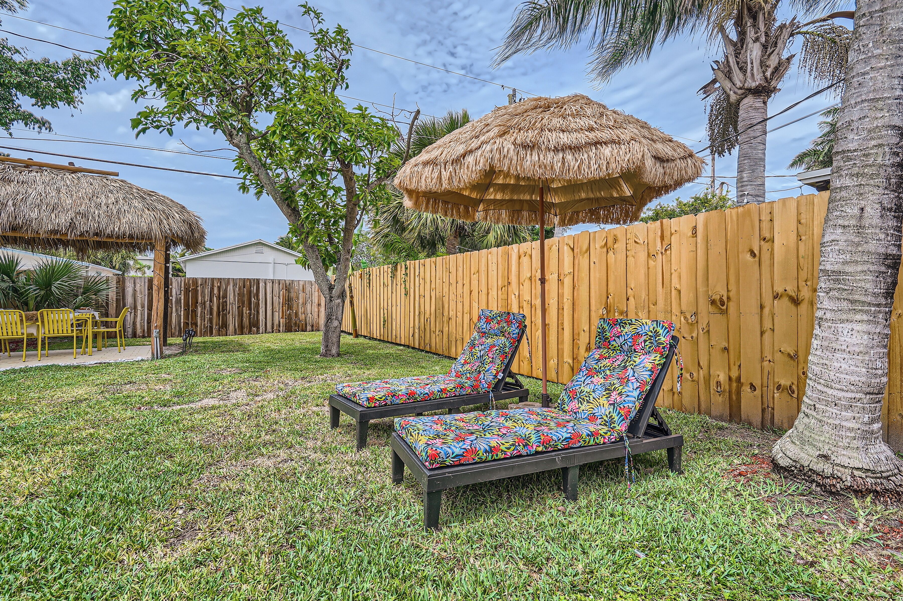 Un patio trasero con dos sillones, un toldo de paja y una valla de madera.