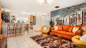 A modern living room with a sofa, armchairs, and a coffee table. There is a kitchen area in the background with a bar and stools. - Spacious 3BR Tropical Retreat - W/Hot Tub Near Beach, Downtown & Airport (West Palm Beach)