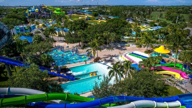 A water park with multiple slides and pools, surrounded by palm trees and buildings. - Spacious 3BR Tropical Retreat - W/Hot Tub Near Beach, Downtown & Airport (West Palm Beach)