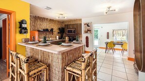 A modern kitchen with a central island, bar stools, and a dining area with yellow chairs. - Spacious 3BR Tropical Retreat - W/Hot Tub Near Beach, Downtown & Airport (West Palm Beach)