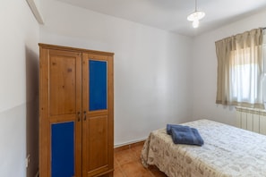 A bedroom with a wooden wardrobe, a bed with a patterned bedspread, and a window with curtains.