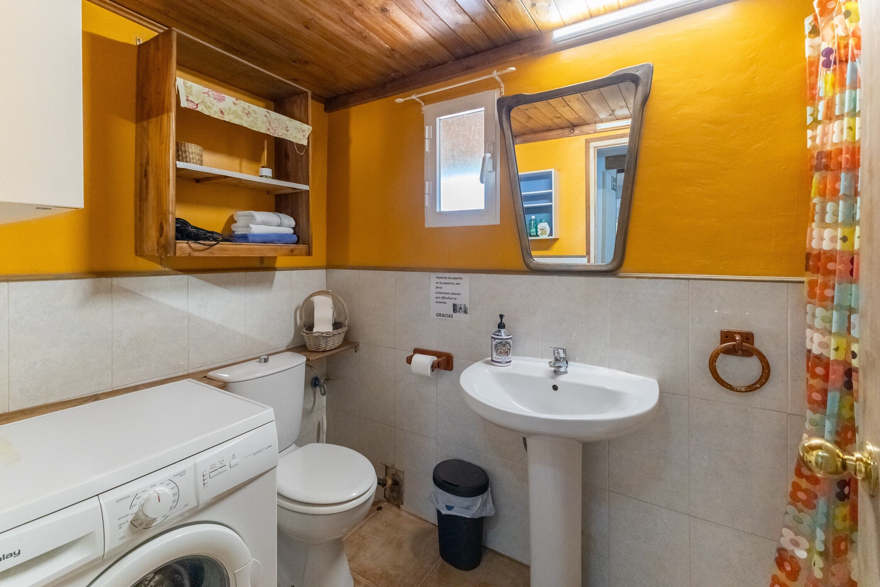 A compact bathroom with a washing machine, toilet, sink, and a mirror.